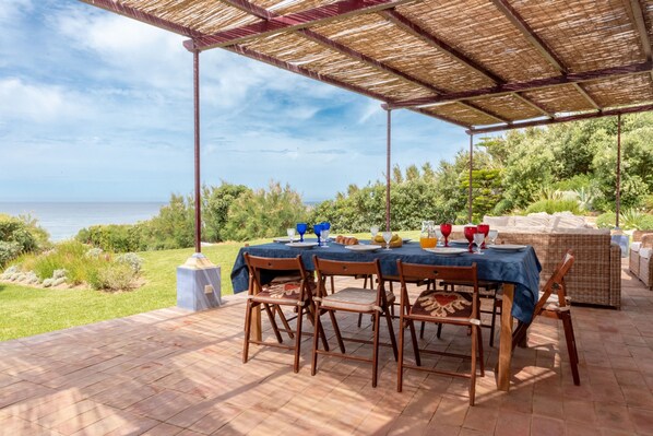 An outdoor dining area with a table set for four, overlooking a scenic view of the sea. - Beachfront Recluse by Cadenzalux (Sintra)