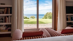 A room with a large window, a bed with striped pillows, and a bookshelf. - Beachfront Recluse by Cadenzalux (Sintra)