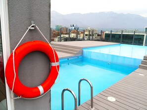 Ein Schwimmbecken mit Rettungsboje, Treppen, die zum Becken führen, und eine Stadtansicht mit Bergen im Hintergrund.