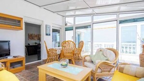 A bright living room with wicker furniture, a television, and a balcony with a view.