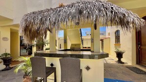 A thatched-roof outdoor bar area with wicker chairs and potted plants.