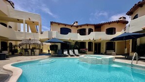 A pool area with a hot tub, lounge chairs, and umbrellas.