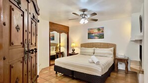 A bedroom with a bed, a ceiling fan, a painting, a wooden wardrobe, and a tiled floor.