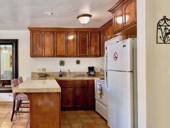 A kitchen with wooden cabinets, a white refrigerator, a coffee maker, and a sink.