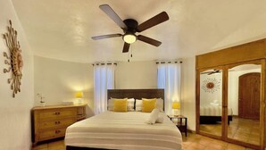 Una habitación de hotel con cama, ventilador de techo, mesita de noche, cómoda y espejo.