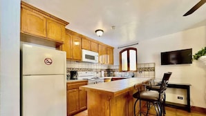 Una cocina con armarios de madera, un refrigerador blanco, un microondas y un salpicadero de azulejos.