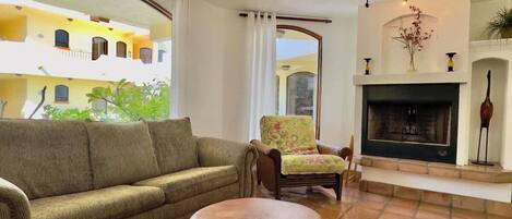 A living room with a sofa, armchair, round ottoman, fireplace, and a ceiling fan.