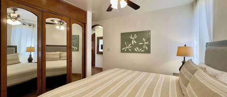 A hotel room with a large bed, a ceiling fan, a wall-mounted artwork, and a mirror.