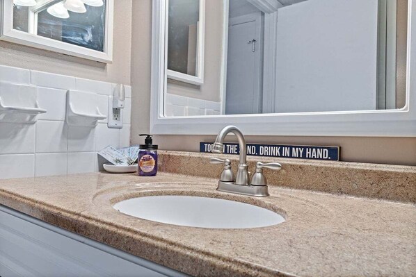 A bathroom with a sink, a mirror, and a sign on the wall.