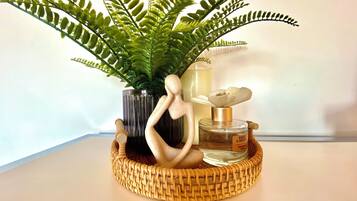 Una cesta de mimbre con una botella de perfume, una figurita decorativa y un helecho en maceta.