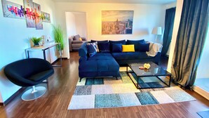 A modern living room with a sectional sofa, a black chair, a coffee table, and a cityscape painting on the wall.