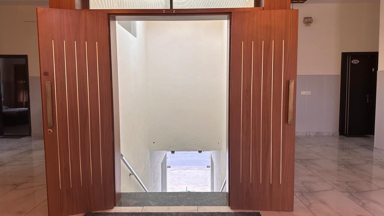Een hotelkamerentree met een houten deur, uitzicht op het strand door een glazen deur en een marmeren vloer.