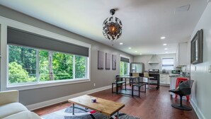 A modern kitchen with a dining area, large windows, and a ceiling light fixture.