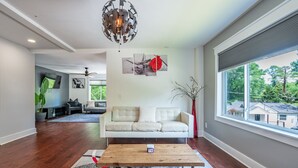 A modern living room with a white sofa, a wooden coffee table, and a large window offering a view of the neighborhood.