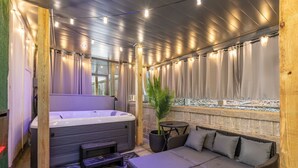 A hot tub area with a sofa and a small table, surrounded by wooden beams and string lights.