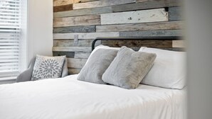A neatly made bed with white bedding and two grey pillows, set against a rustic wooden headboard. - 2 Bedroom Loft Style Home in ATL near Downtown (Atlanta)