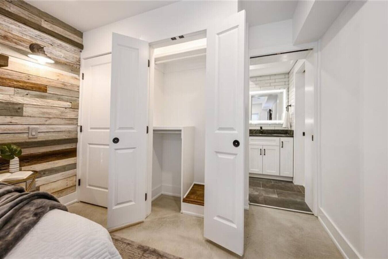 Een slaapkamer met een bed, nachtkastje en nachttafel. Aan één kant van de kamer is houten wandbekleding.