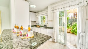 Une cuisine moderne avec des meubles blancs, un plan de travail en granit et une vue sur un jardin, visible à travers des portes vitrées.
