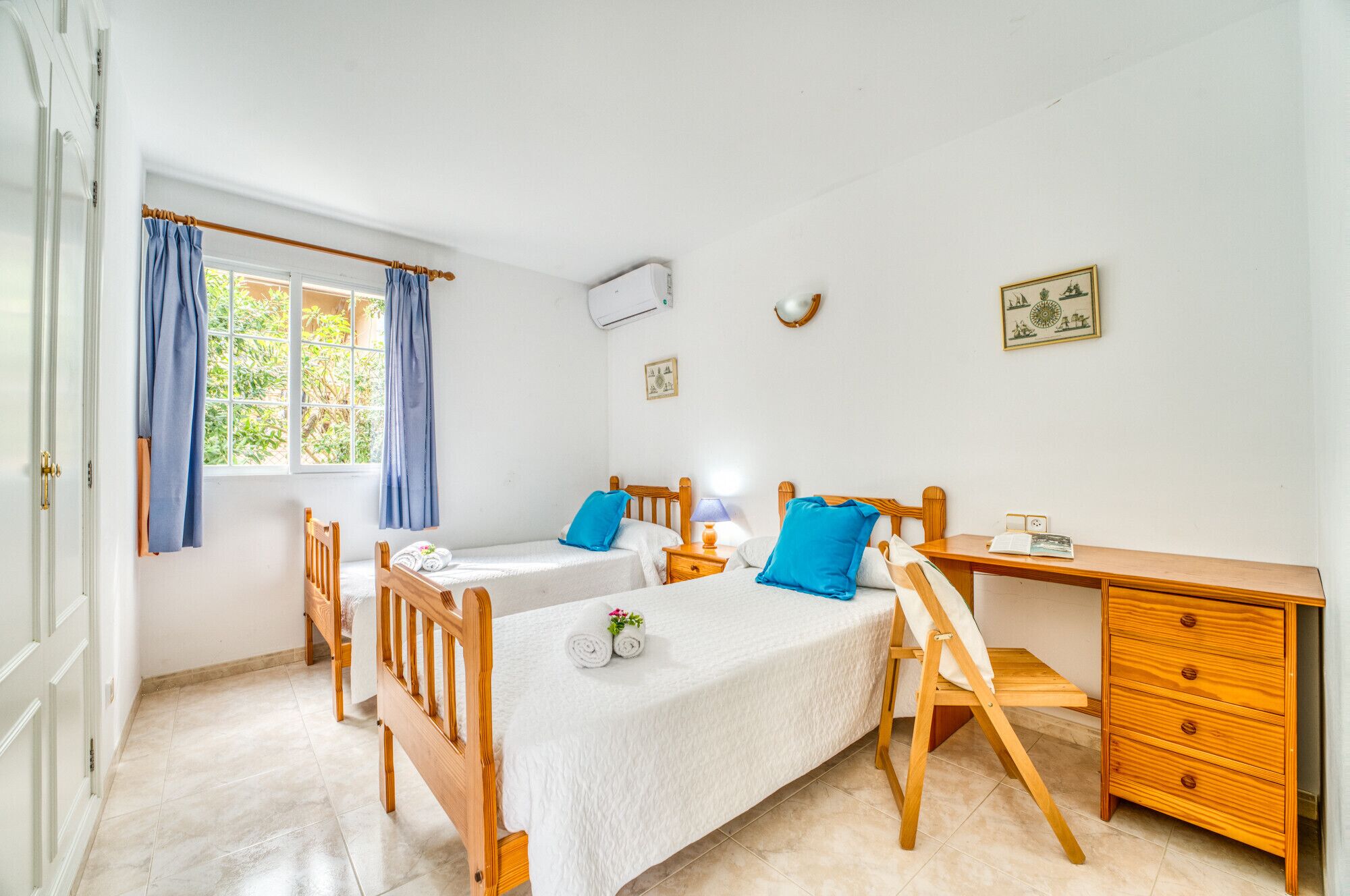 Ein Zimmer mit zwei Einzelbetten, einem Holztisch, einem Stuhl, einem kleinen Tisch und einer Kommode.