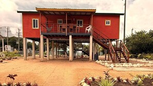 Un edificio de dos pisos con fachada roja, un porche cubierto y una escalera que lleva al nivel superior.