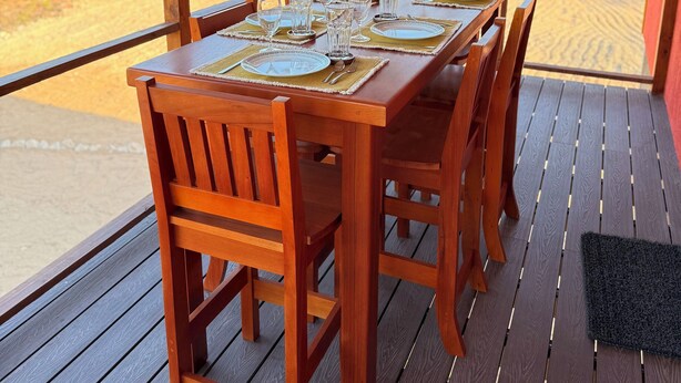 Una terraza de madera con una mesa dispuesta para comer, rodeada de sillas y un ventilador de techo.