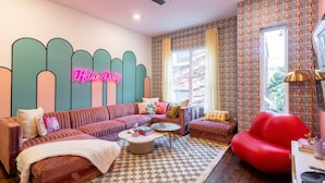 A cozy living room with a neon sign, patterned wallpaper, and a checkered rug. - The Dolly Den! • Murals and Glam | Private Rooftop (Nashville)