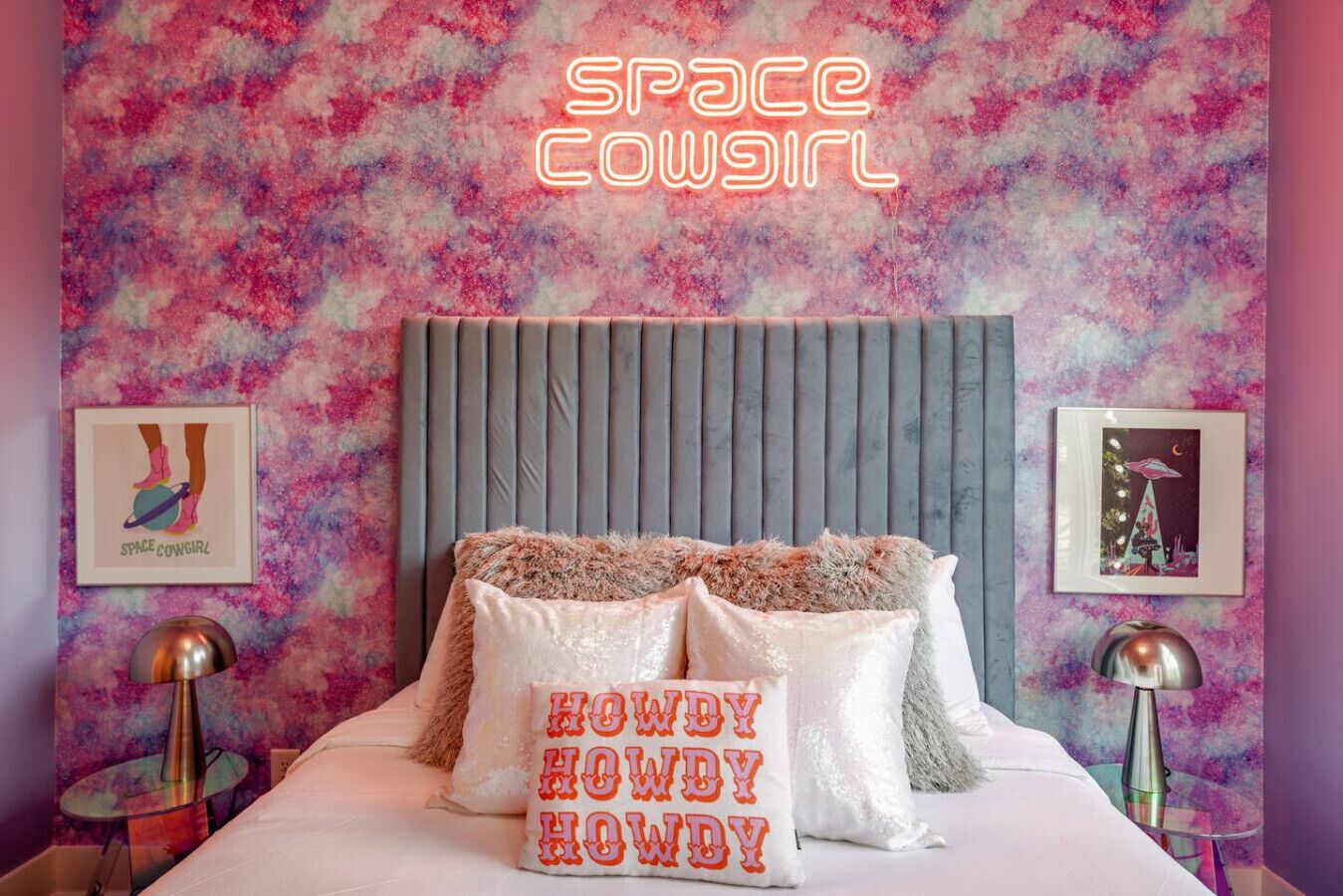 A bedroom with a pink and purple abstract wall design, a grey headboard, and two bedside lamps.