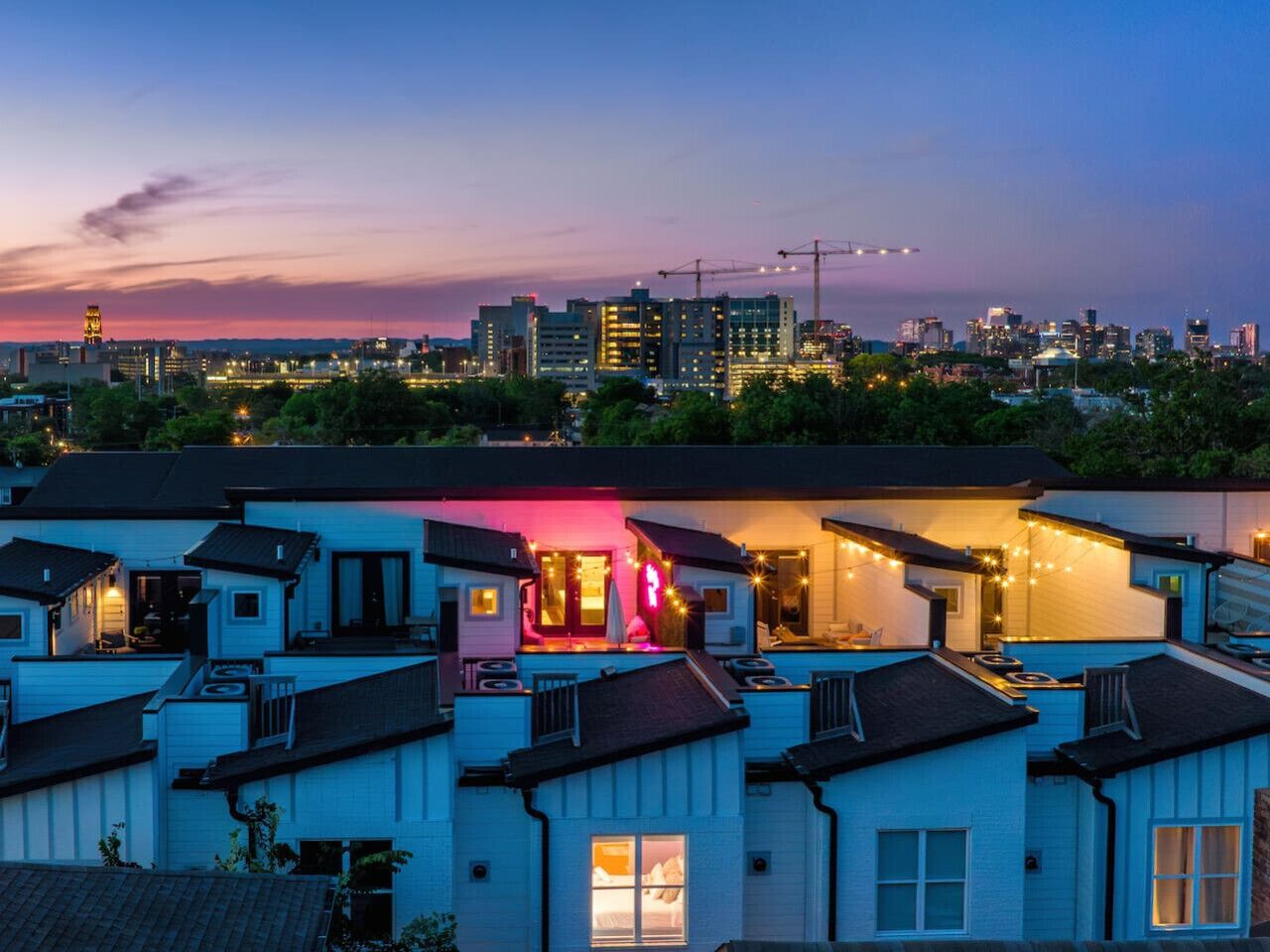 Un barrio residencial con varias casas, algunas con balcones a la vista y un edificio destacado con entrada iluminada en rosa.