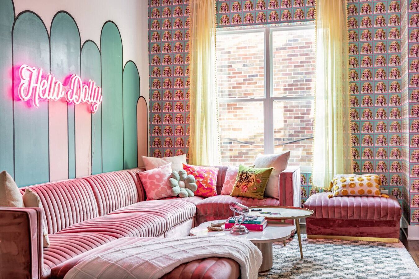 Un salon chaleureux avec un canapé rose, une table basse ronde et un panneau lumineux au néon sur lequel on peut lire « Bonjour Dolly ».