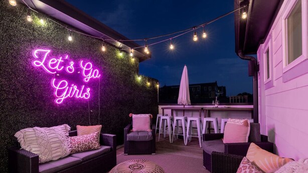 An outdoor seating area with a neon sign, wicker furniture, and a bar. - The Dolly Den! • Murals and Glam | Private Rooftop (Nashville)