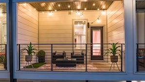 A two-story building with a balcony featuring a sofa, two potted plants, and string lights. - The Dolly Den! • Murals and Glam | Private Rooftop (Nashville)