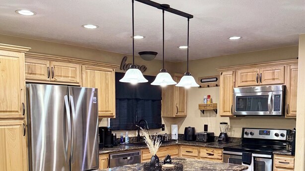A modern kitchen with stainless steel appliances, wooden cabinets, a granite countertop, and pendant lighting.