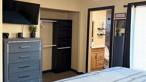 A bedroom with a bed, a dresser, a ceiling fan, a TV, and a door leading to another room.