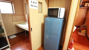 A compact room with a sink, a microwave on a small fridge, and a sign indicating a bathroom. - Guest House Aman (Amami)