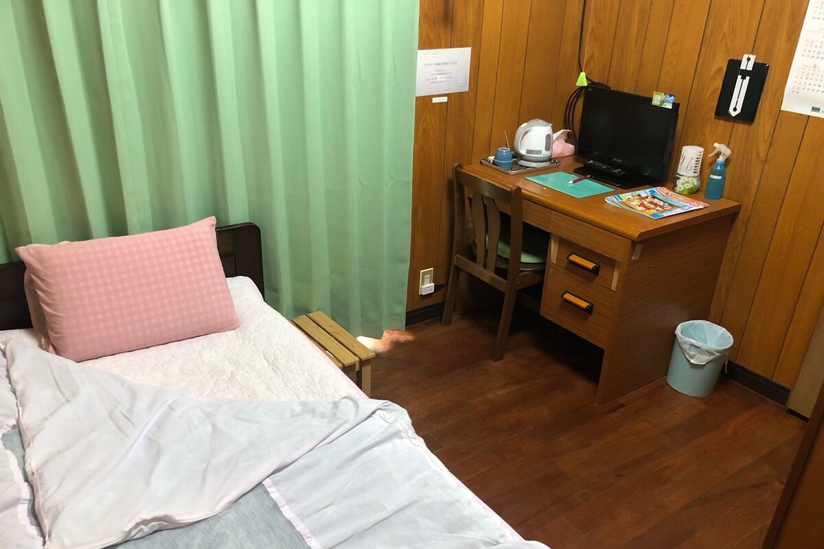 A hotel room with a bed, a desk with a computer, a chair, and a trash bin.