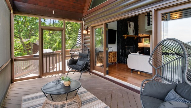 A wooden deck with a round table and two chairs, a view of the outdoors, and a glimpse of the interior. - Discover Modern Luxe Vibes • HotTub • PoolTable • Secluded (Blue Ridge)