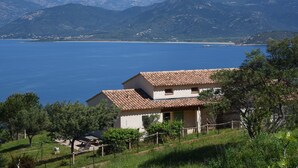 Une maison avec un toit en tuiles, donnant sur un lac et des montagnes.