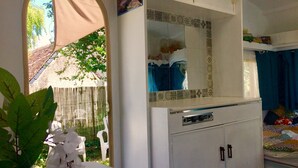 Une pièce avec une armoire blanche, un miroir, une petite table sur laquelle est posé un vase de fleurs, et un lit avec un rideau bleu.