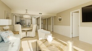 Ett rymligt vardagsrum med en matplats, ett kök i bakgrunden och en stor TV som är monterad på väggen.