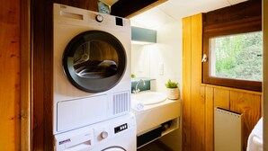 Ein kleines Badezimmer mit Holzvertäfelung, einer Frontlader-Waschmaschine, einem Waschbecken, einem kleinen Fenster und einer Heizung.