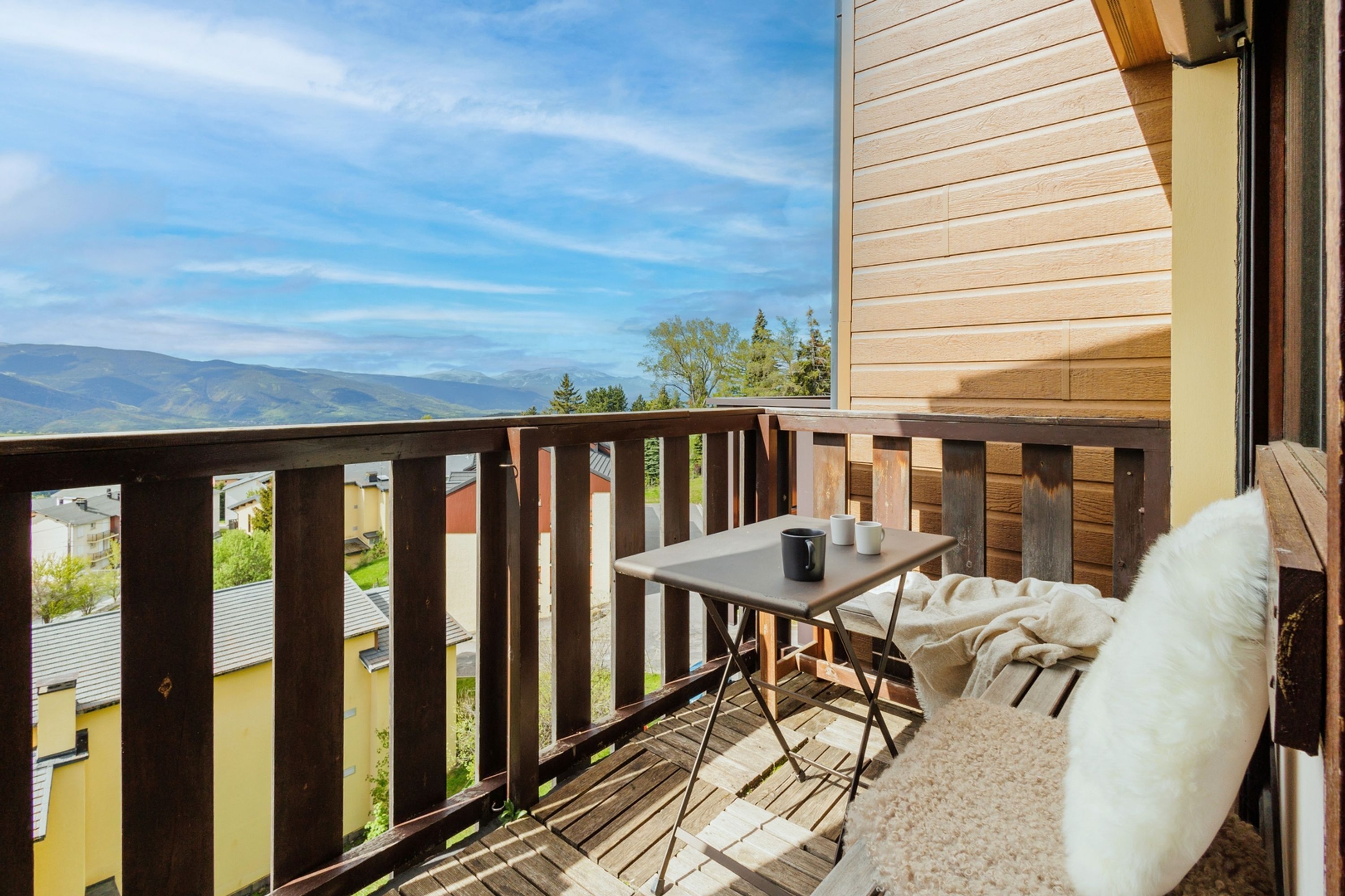 A balcony with a wooden railing, a small table with cups, and a white cushion.