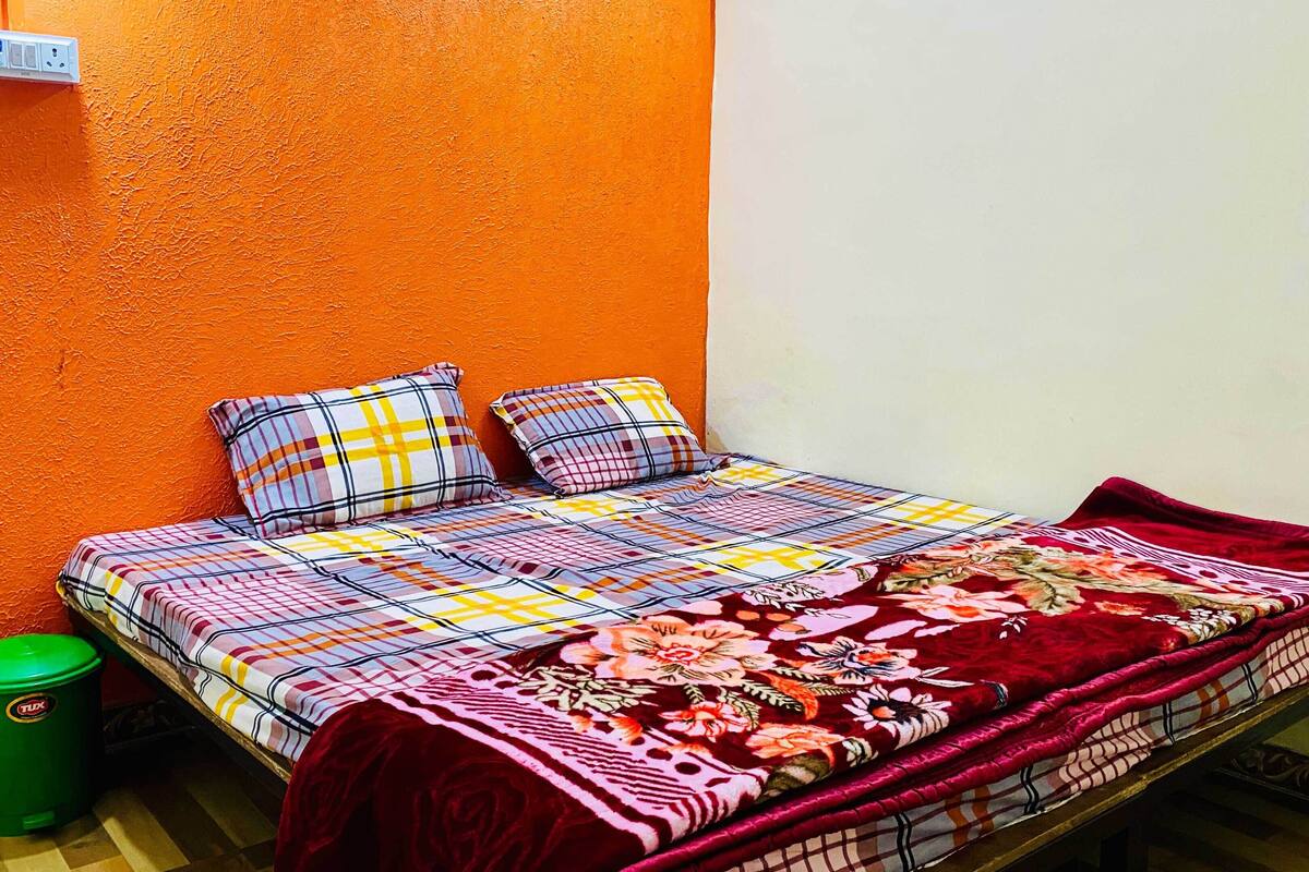 A single bed with a colorful quilt and two pillows, a green trash bin, and a tiled floor.
