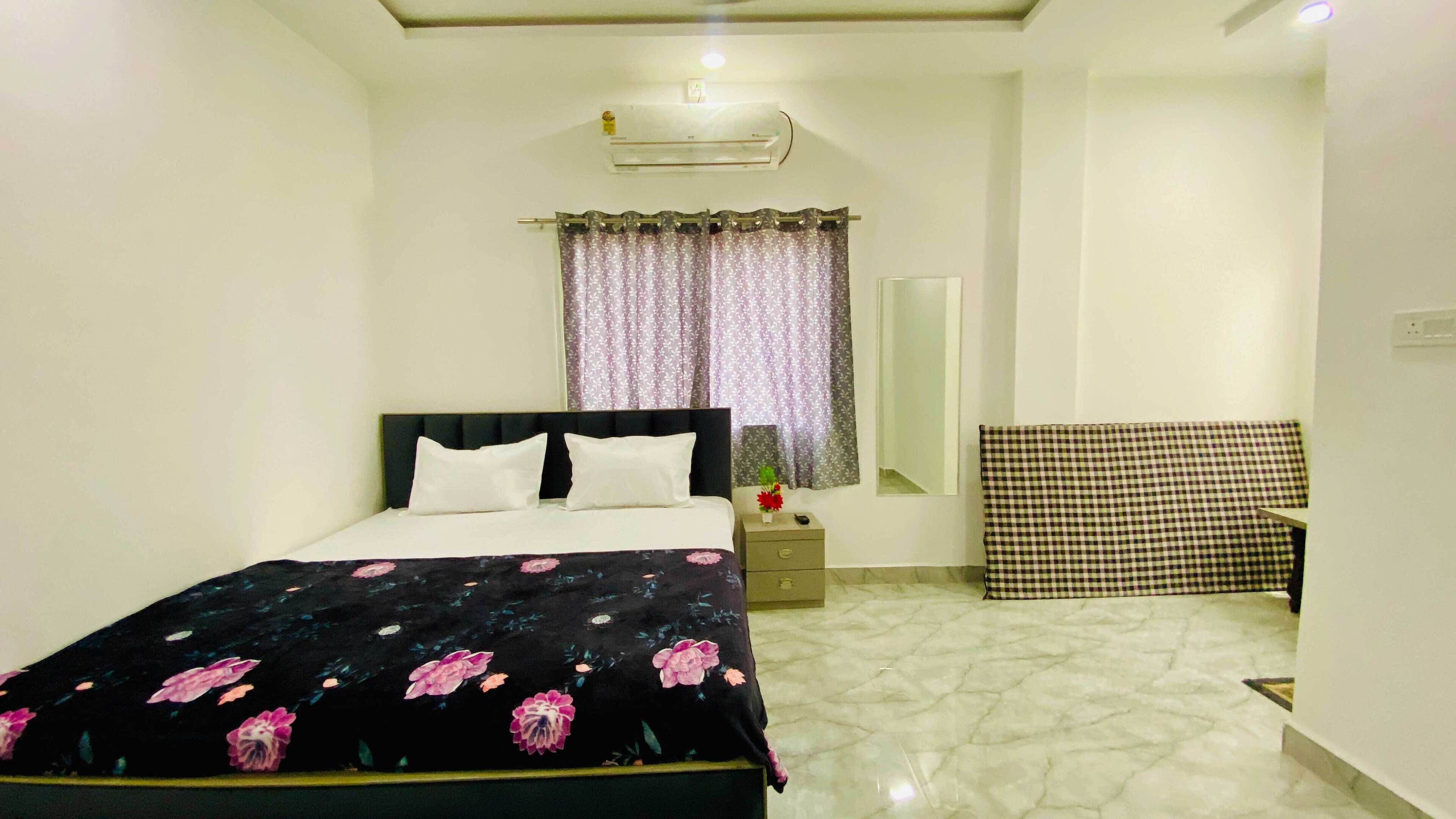 A bedroom with a bed, a nightstand, a mirror, a checkered chair, and a window with curtains.