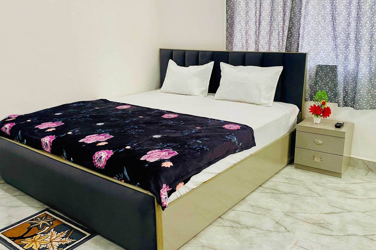 A neatly made bed with a floral bedspread, a bedside table with a vase of flowers, and a marble floor.