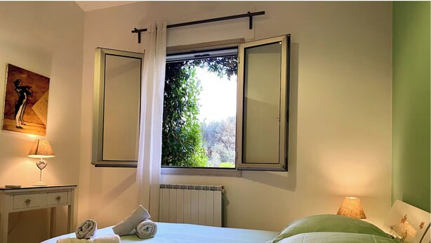 A hotel room with a bed, a desk with a lamp, a radiator, and a window with curtains. - Charming apartment (Allauch)