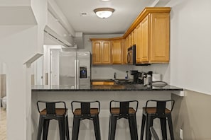 Una cocina con armarios de madera, encimera negra y tres taburetes negros.