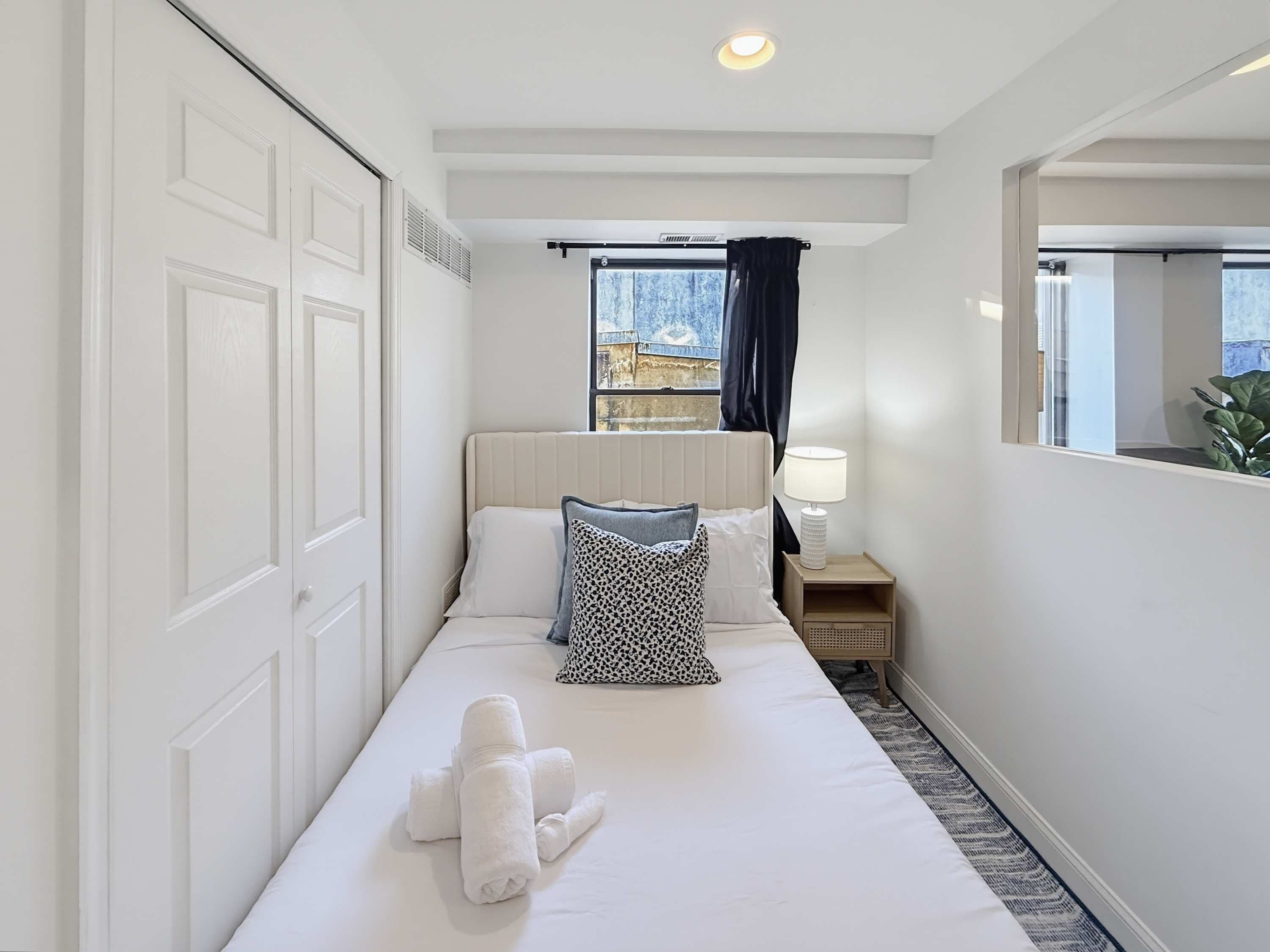 A hotel room with a bed, a nightstand, a lamp, a window with curtains, and a view of the outside.