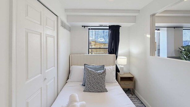 A hotel room with a bed, a nightstand, a lamp, a window with curtains, and a view of the outside.