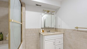 A bathroom with a glass shower enclosure, a white sink with a mirror above it, and beige tiled walls.