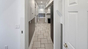 A hallway with white walls, a tiled floor, and a door with a brass handle.